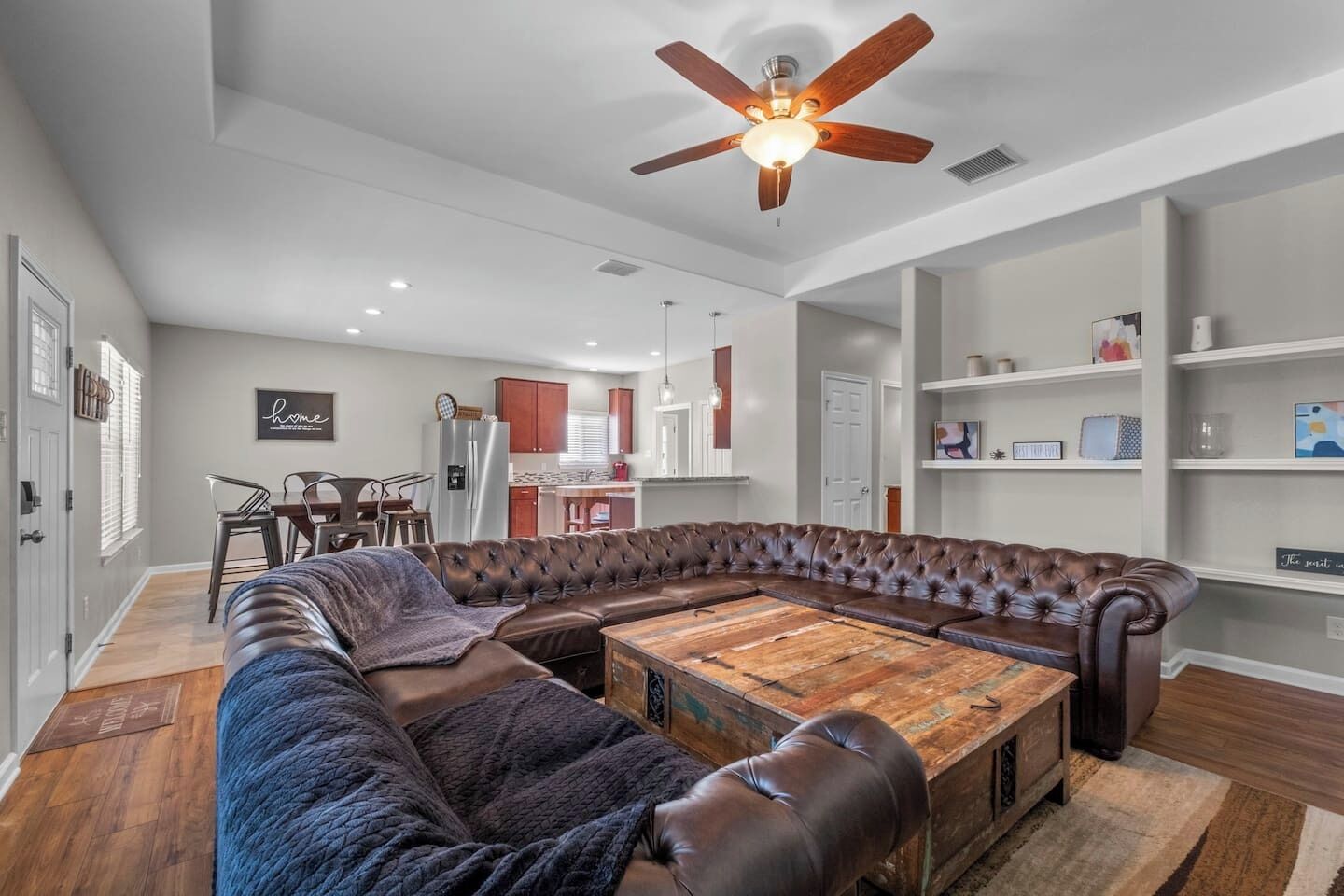 Ein modernes Wohnzimmer mit einem Ecksofa, einem Holztisch und einem Deckenventilator.