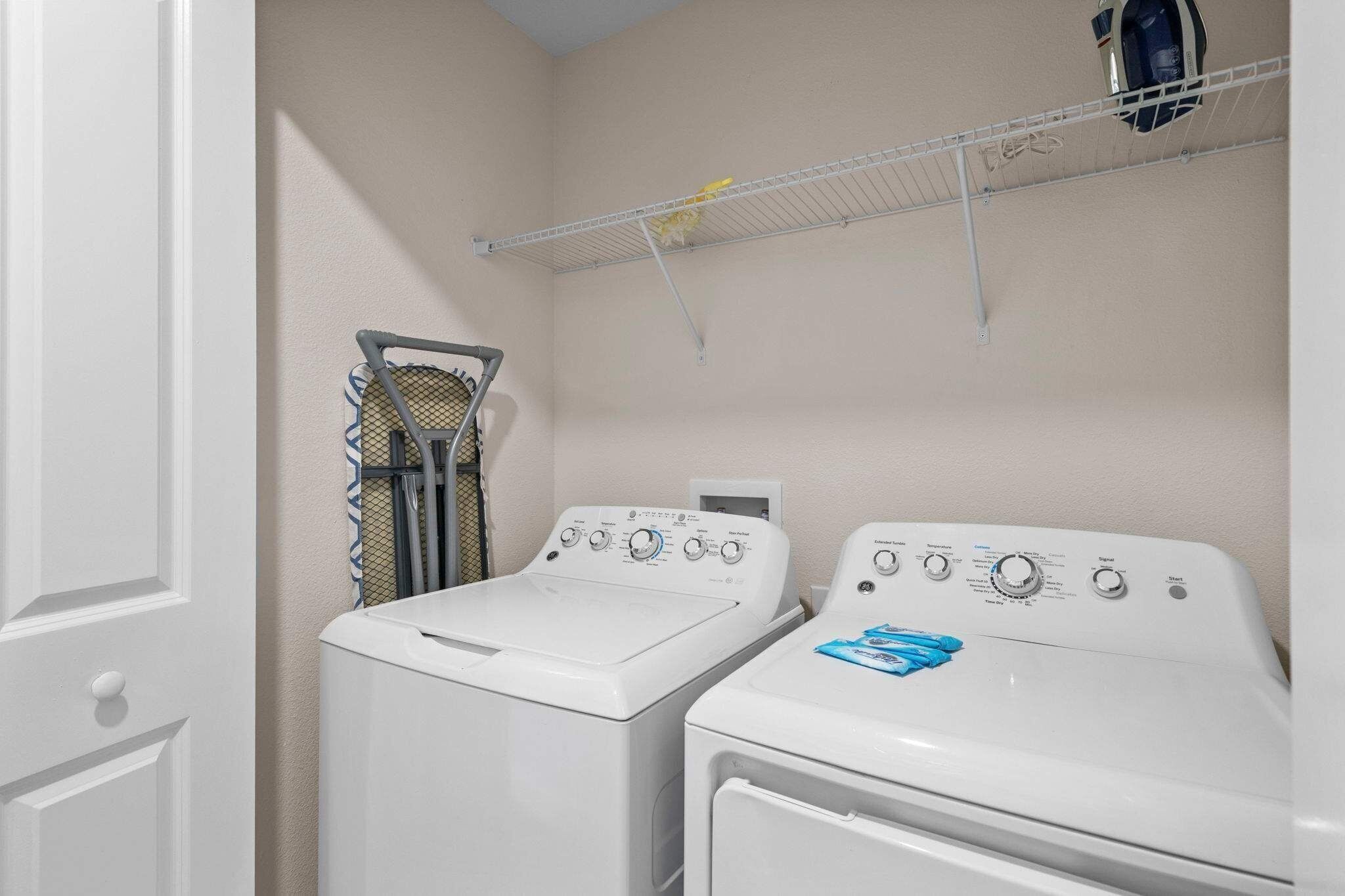 A laundry room with two front-loading washers and dryers, a metal shelf with a basket, and a ceiling-mounted rack.