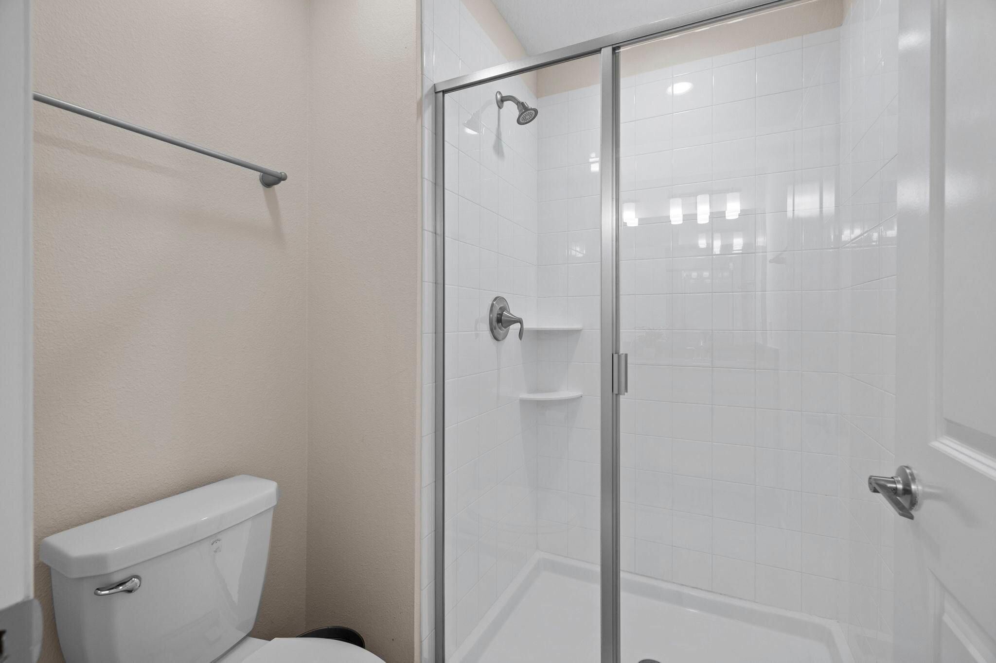 A bathroom with a glass-enclosed shower, a toilet, and a towel rack.