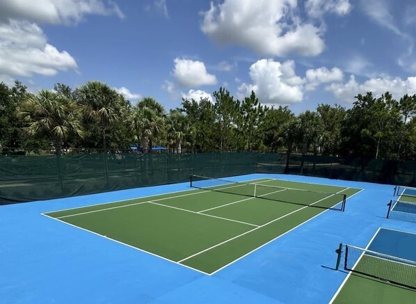 A tennis court with a net, surrounded by a fence and trees.