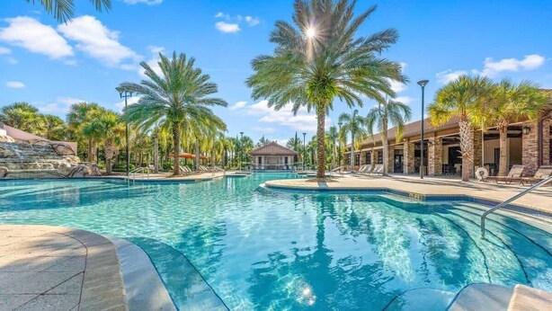 A swimming pool with palm trees, a stone building, and a clear blue sky.