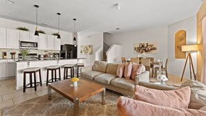 A modern kitchen with white cabinets, a central island with stools, and pendant lighting.