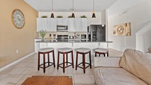 A modern kitchen with white cabinets, a central island with bar stools, and pendant lighting.