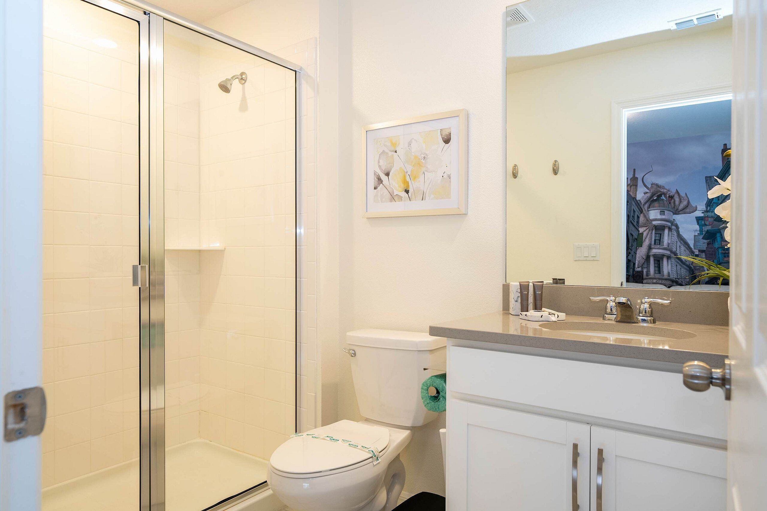A bathroom with a glass shower enclosure, a toilet, and a sink with a mirror above it.