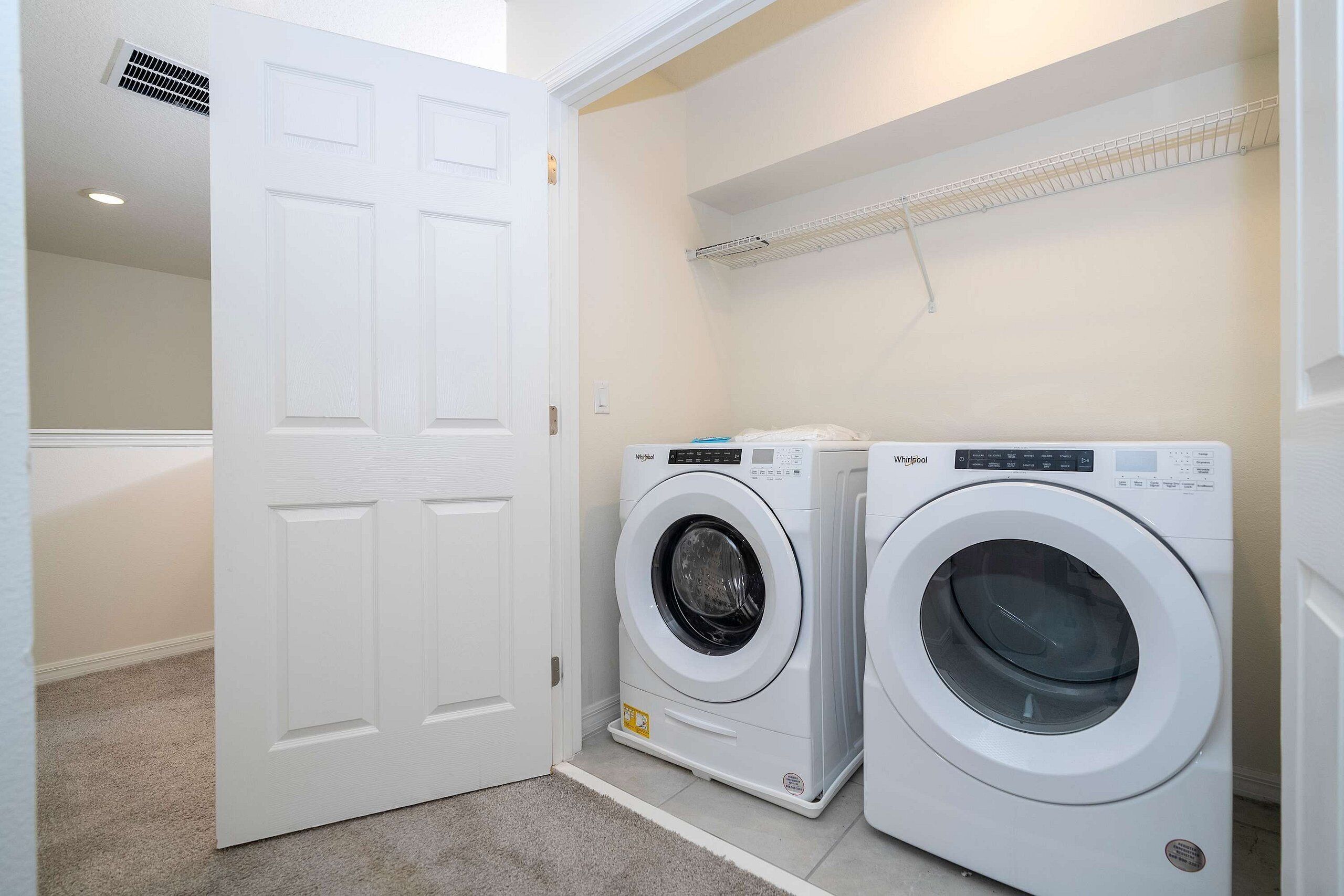 A laundry room with two front-loading washing machines, a white door, and a ceiling vent.