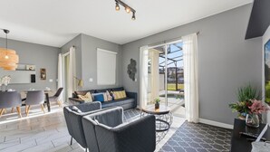 En moderne stue med sofa, stole, spiseplads og udsigt til det fri gennem en glasdør.