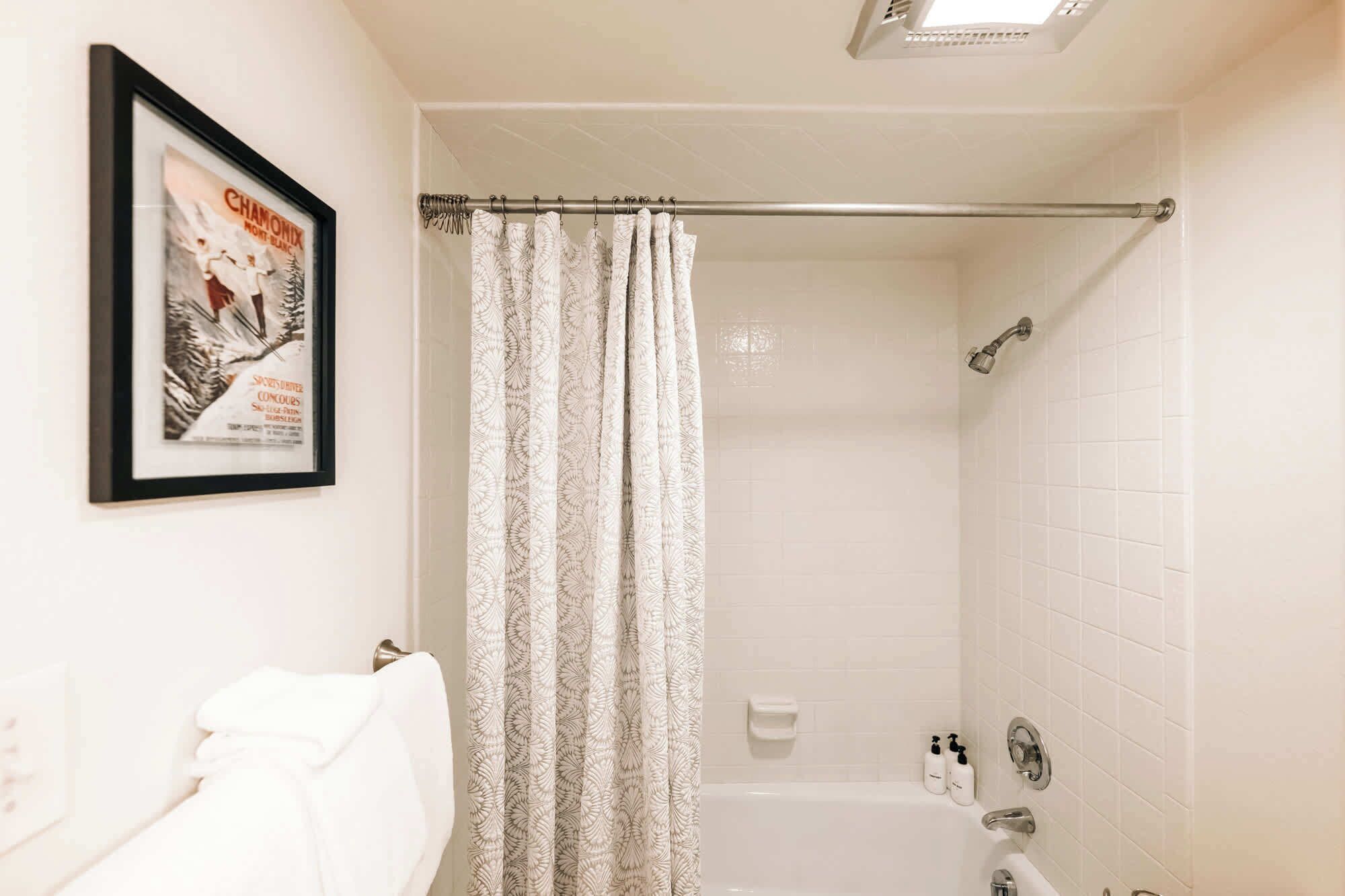 A bathroom with a shower, a framed poster on the wall, and a towel rack.