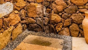 A stone wall with a metal structure, possibly a water feature, and a rustic building in the background. - CASA GUATI (Barichara)