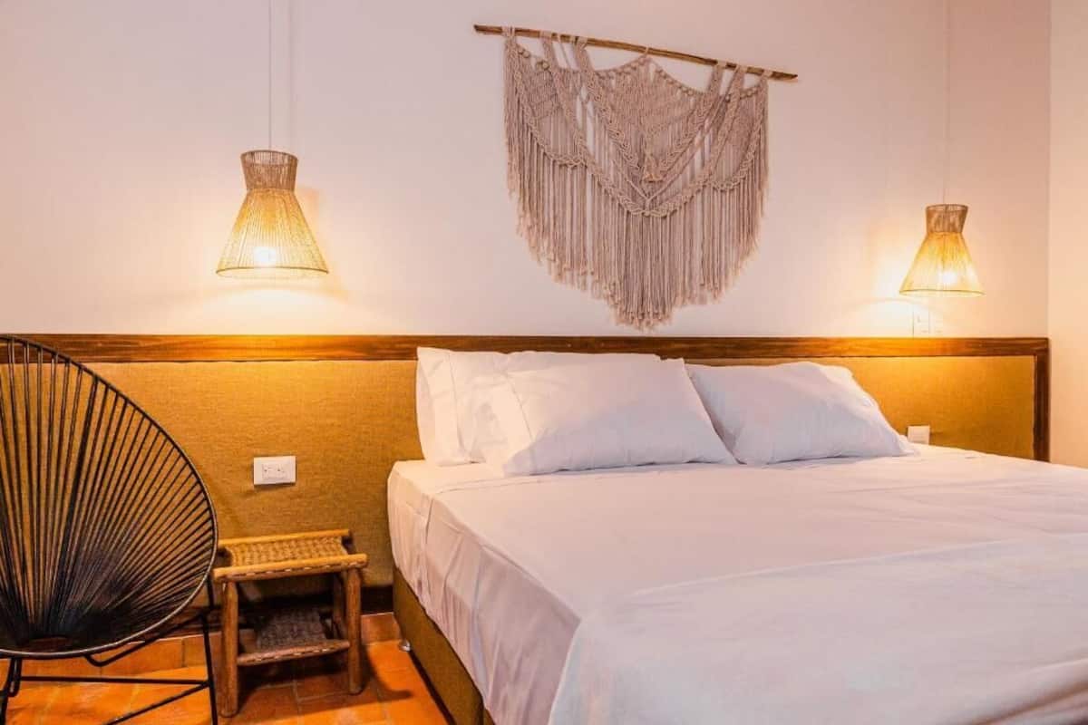 Una cama con ropa blanca, un cabecero de madera y dos lámparas fijadas a la pared.