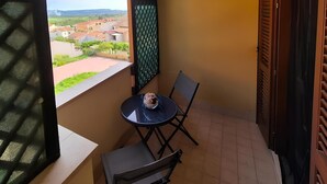 Ein kleiner Balkon mit Tisch und Stühlen, Blick auf eine Wohngegend und eine Tür mit Fenster.