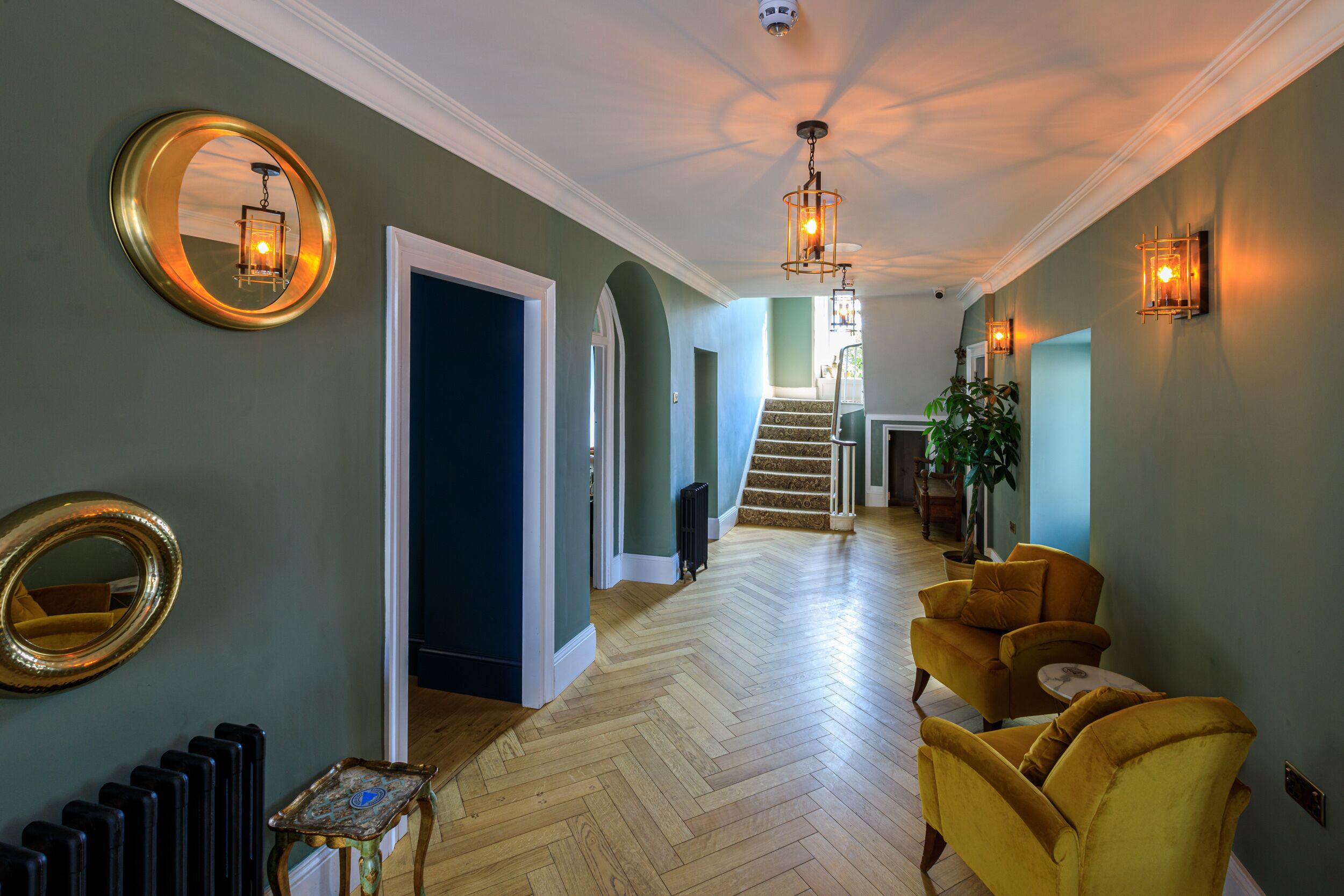 A hallway with a herringbone floor, a staircase, and a seating area with yellow chairs.
