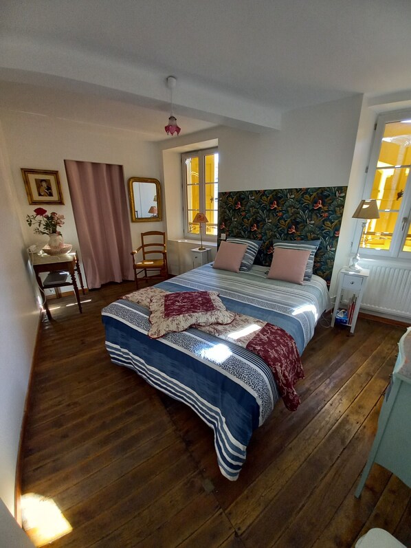 A bedroom with a bed, a chair, a desk, a window, and a mirror.