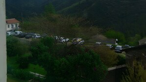 Une vue d’un paysage montagneux, avec une maison et des voitures garées au premier plan.