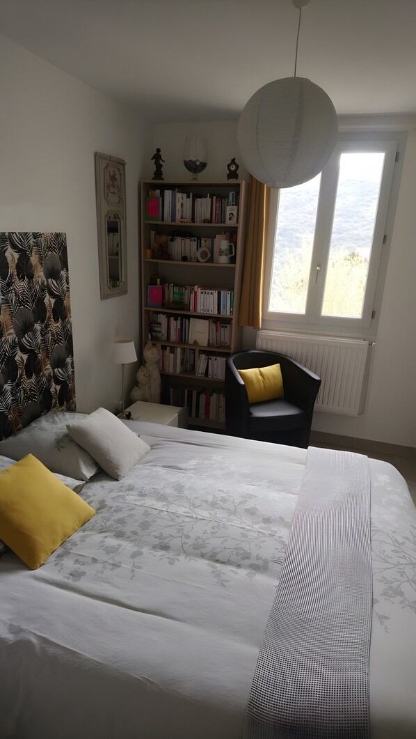 Ein Schlafzimmer mit Bett, Bücherregal, Sessel und Fenster.