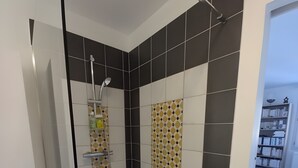 Une salle de bain moderne avec une douche, des carreaux blancs et noirs, et une porte en verre donnant sur une chambre.