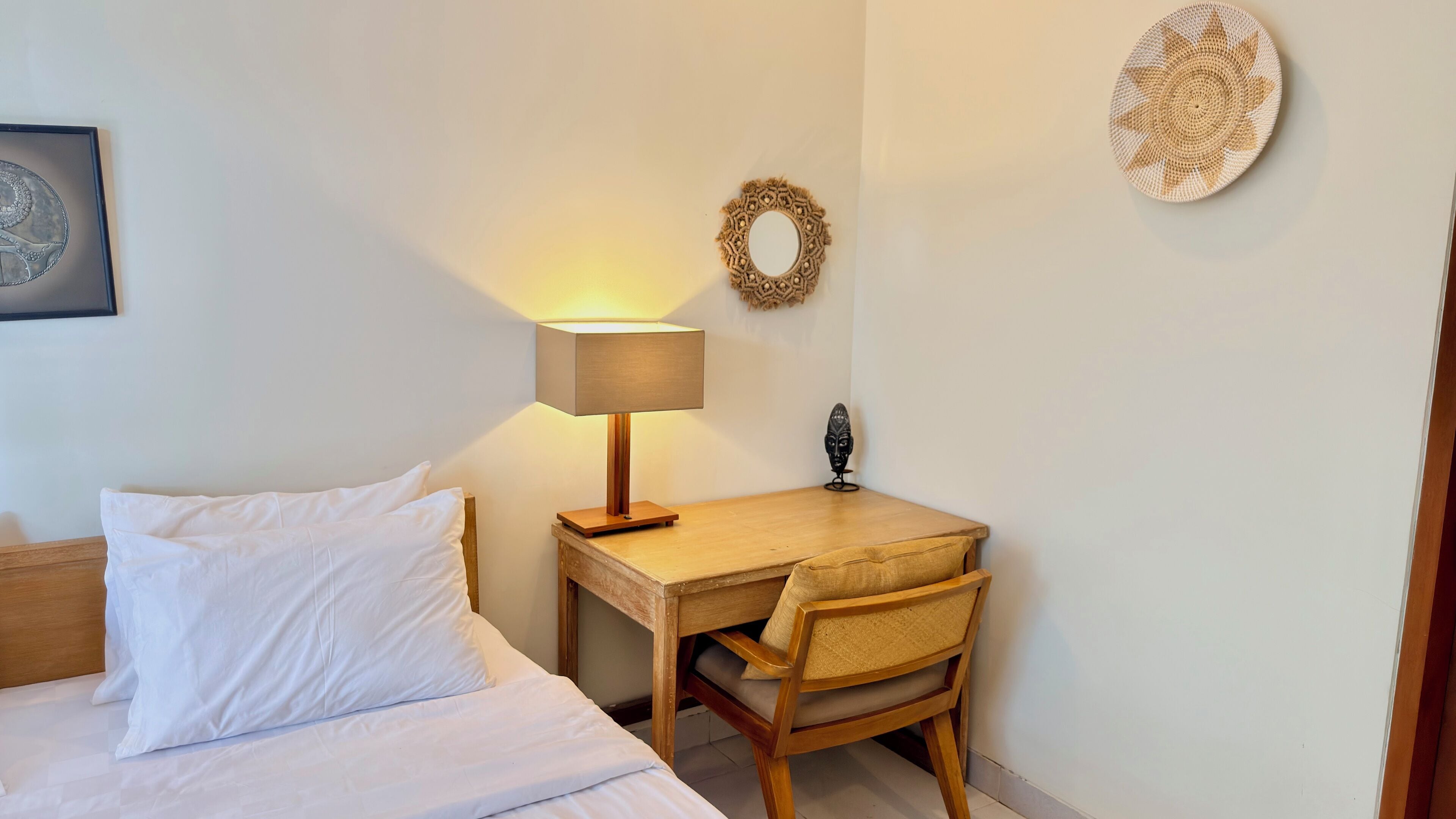 Un lit bien fait, avec du linge de lit blanc, une table de chevet en bois avec une lampe, une petite table en bois et une chaise.