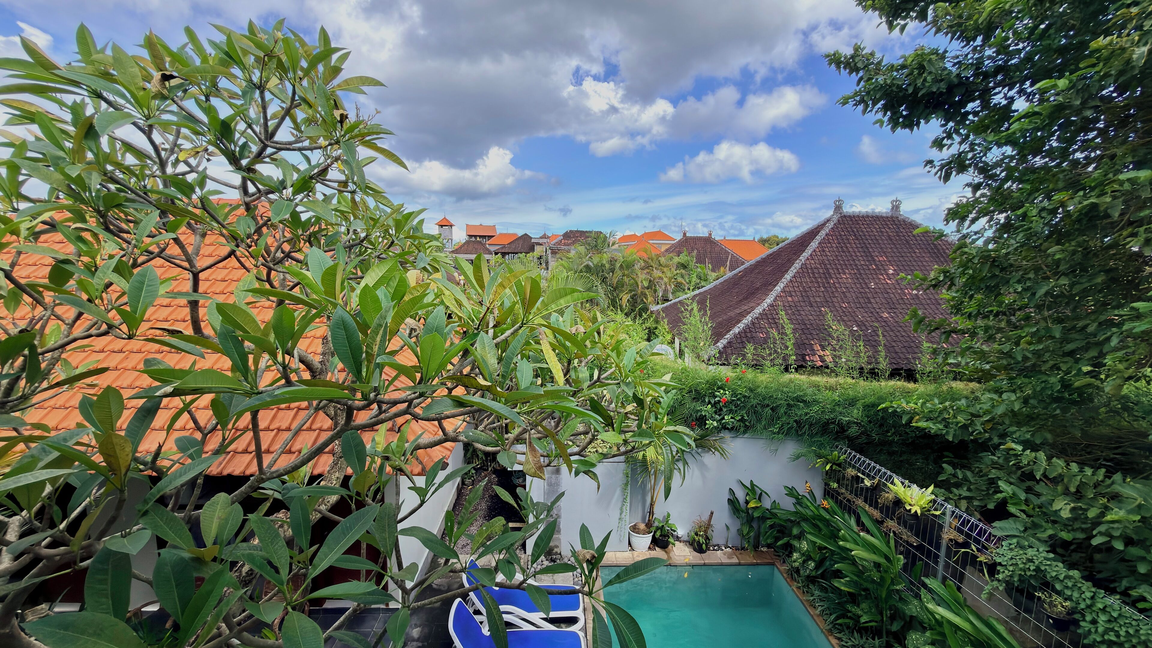 Una piscina rodeada de exuberante vegetación y casas tradicionales con techos de tejas rojas.