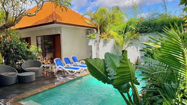 Ein Poolbereich mit Liegestühlen, einer überdachten Lounge und üppiger tropischer Bepflanzung.