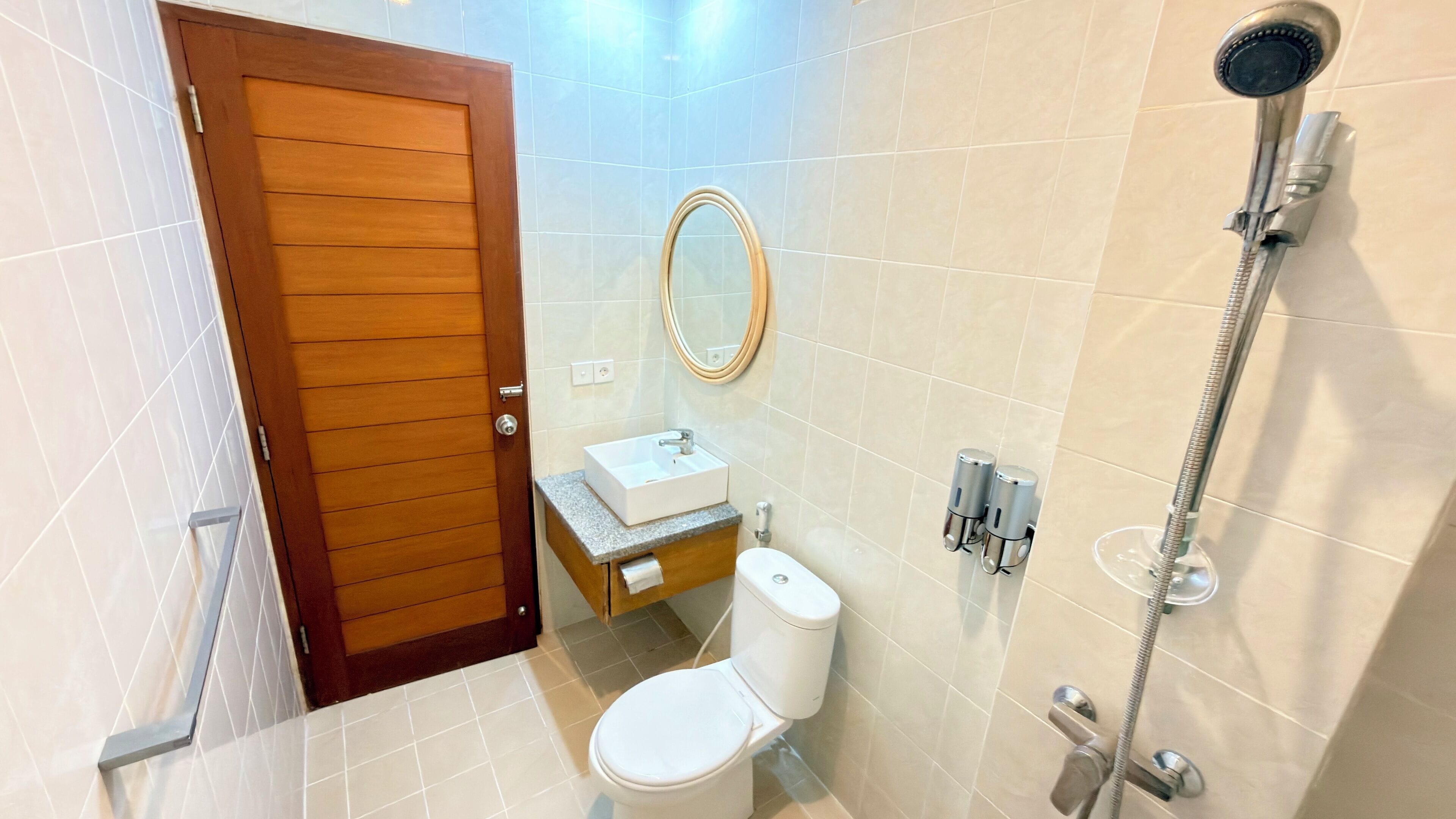 Un bagno con porta in legno, lavandino bianco, un water, uno specchio e una doccia.