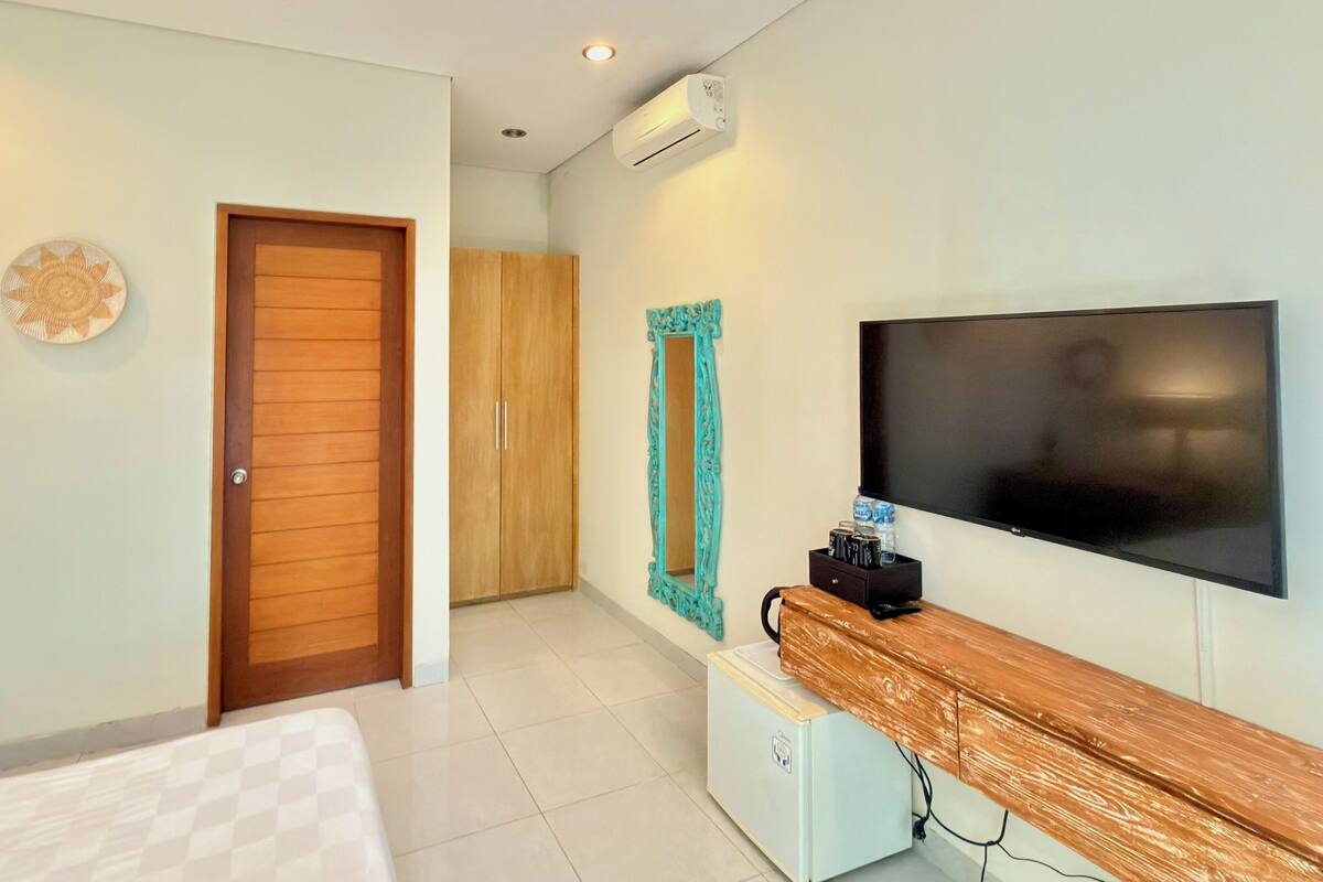 Habitación de hotel con cama, armario de madera, televisor y un pequeño escritorio con una botella de agua y latas.