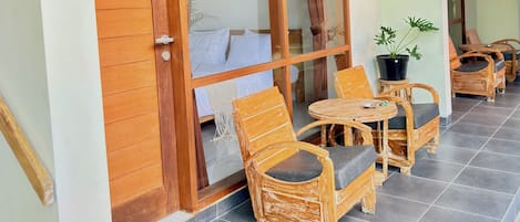 Una puerta de madera con un panel de vidrio, sillas de mimbre, una mesa redonda pequeña y una planta en maceta.