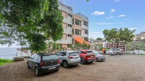 A parking area with multiple cars, a building with balconies, and a view of the sea. - Holiday Studio 'Estudio Alenia' (San Marcos)