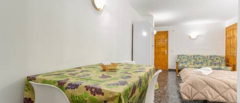 A room with a dining table, chairs, a bed, and a small sofa.