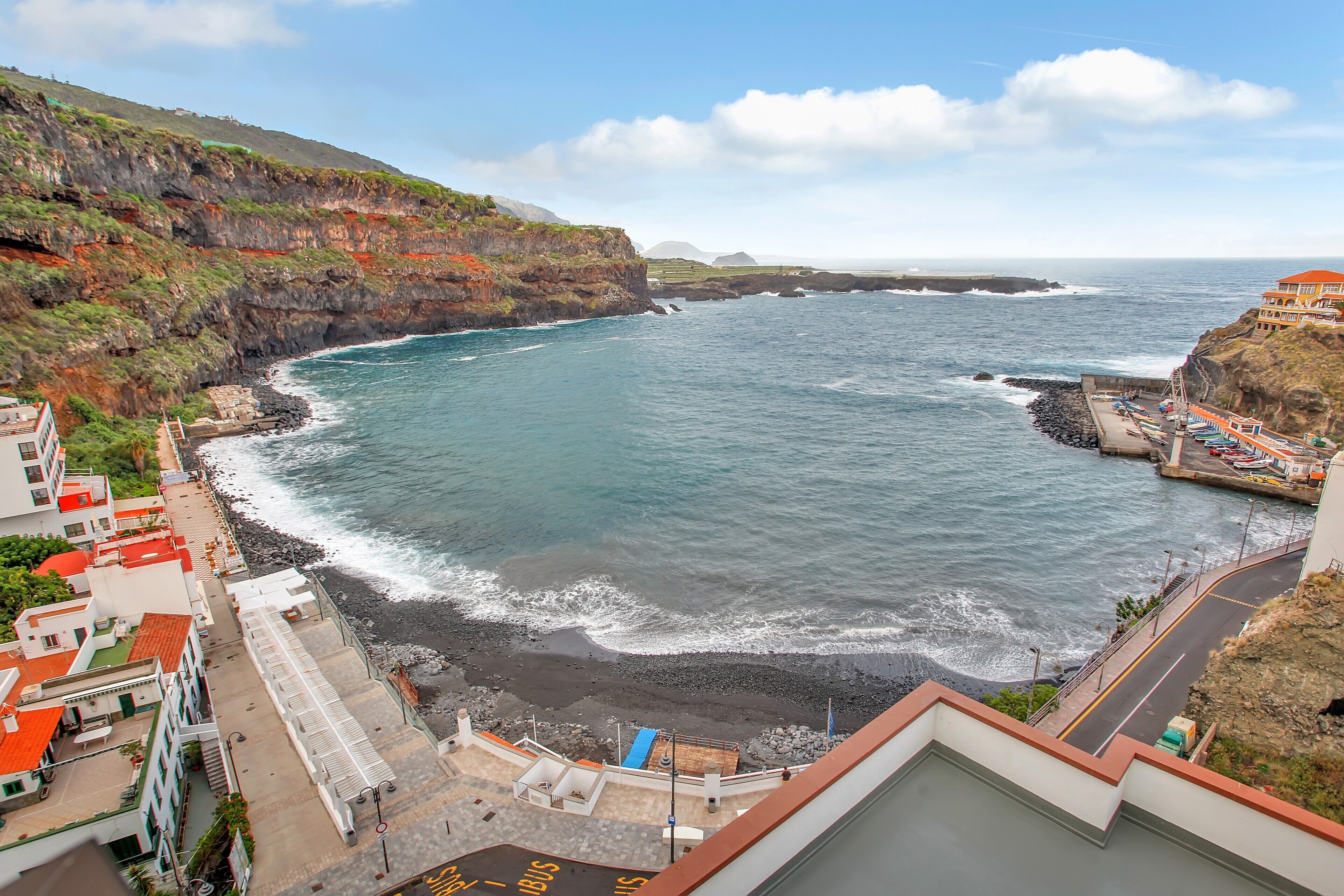 Un hotel costero con vistas al mar, un estacionamiento y una carretera que lleva a la playa.