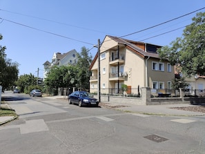 A residential street with a two-story apartment building, a car parked on the side, and a pedestrian crossing.