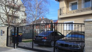 A gated entrance with two parked cars, a stone wall, and a building with balconies in the background. - Spacious 6-bedroom apartment in welcoming Budapest with AC (Budapest)