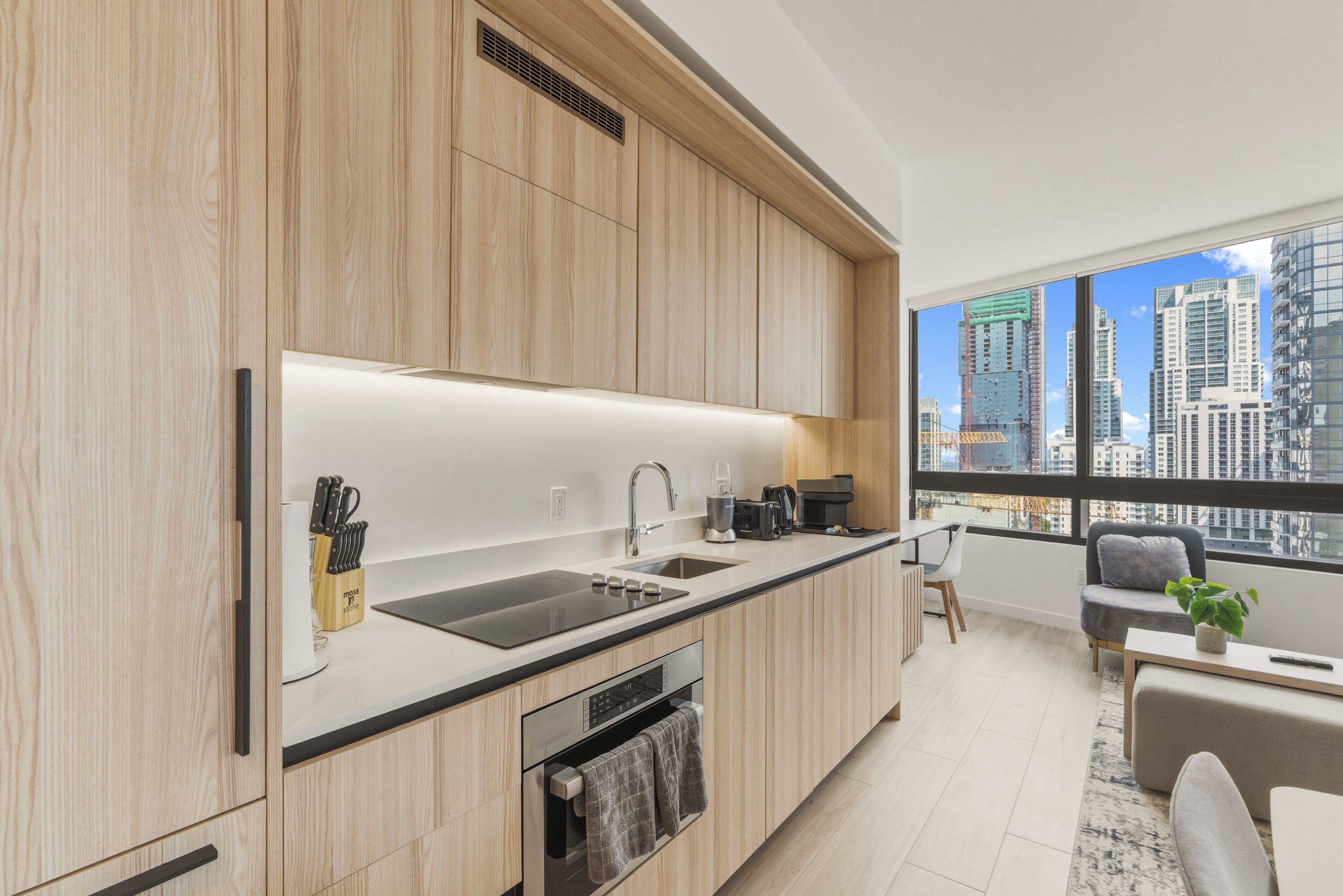 A modern kitchen with a large window, a dining area, and a view of the cityscape.