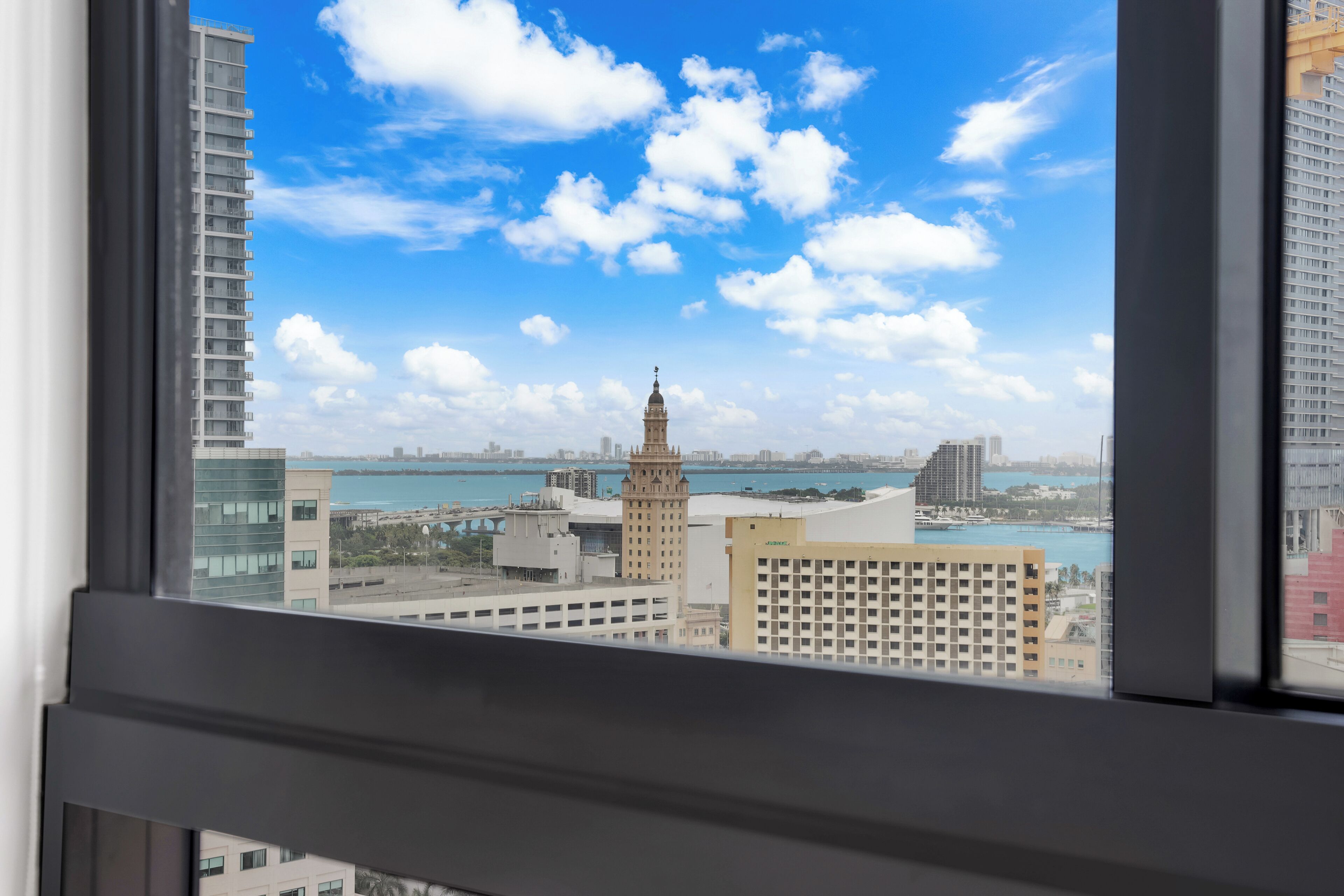 A view from a window overlooking a cityscape with a prominent tower and a body of water.