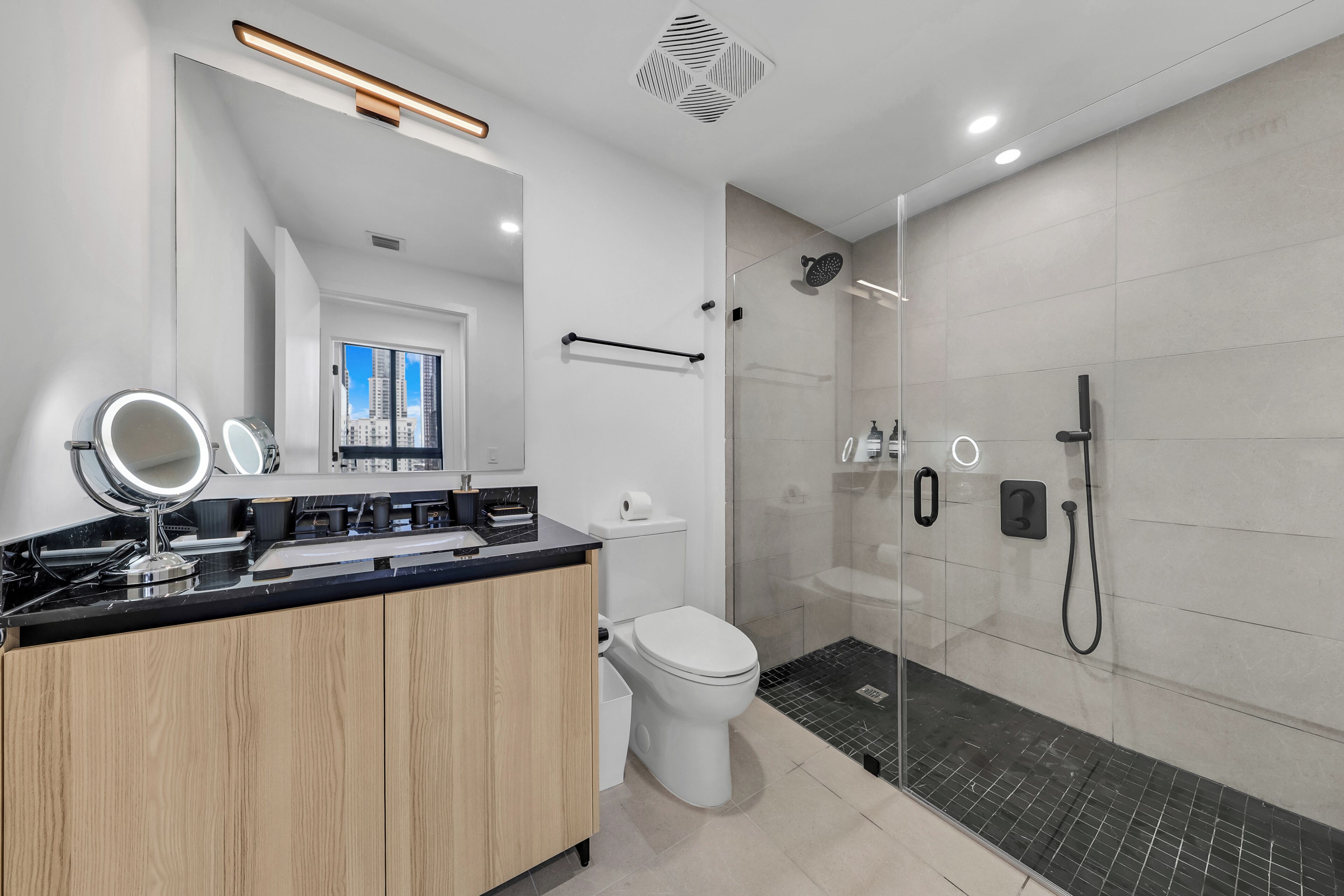 Une salle de bain moderne avec une douche à parois de verre, un meuble-lavabo en bois, un miroir avec éclairage intégré et des toilettes.