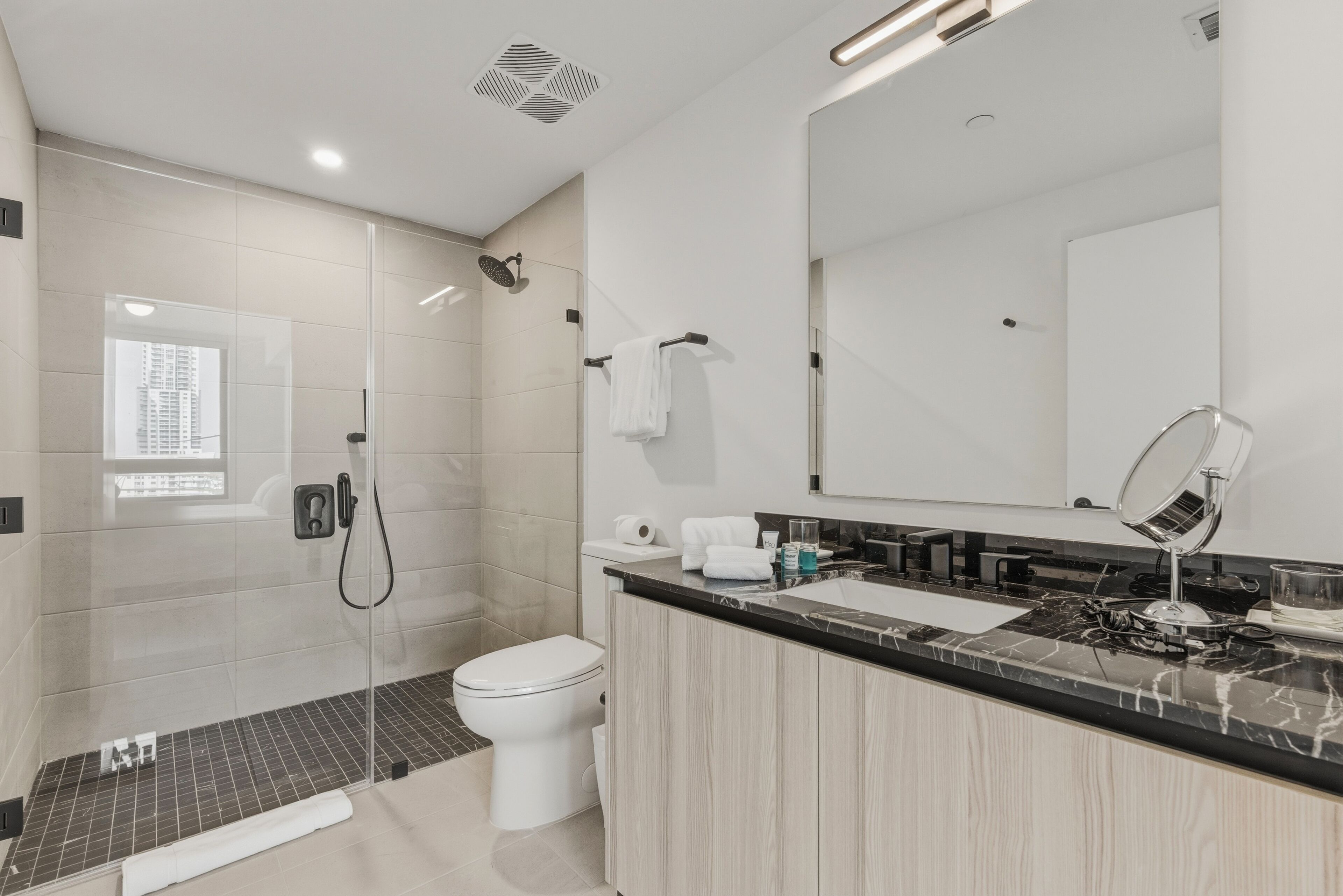 Un bagno moderno con cabina doccia in vetro, un water, un lavandino con specchio e una finestra che offre luce naturale.