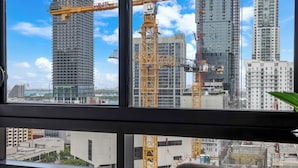Vista attraverso una finestra su una città con gru, grattacieli e cielo sereno.