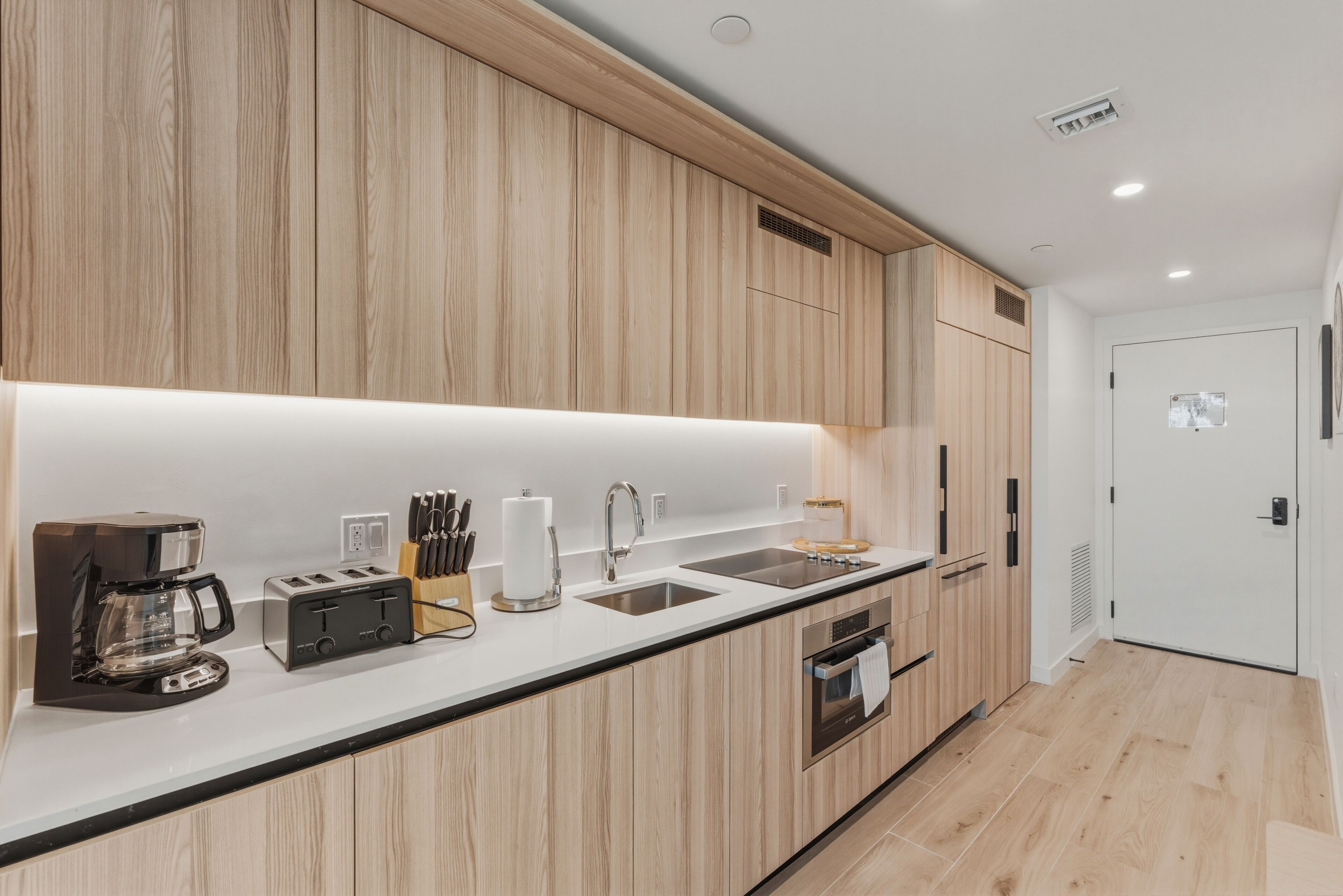 Una cocina moderna con armarios de madera, encimera blanca, cafetera, tostadora y pileta.