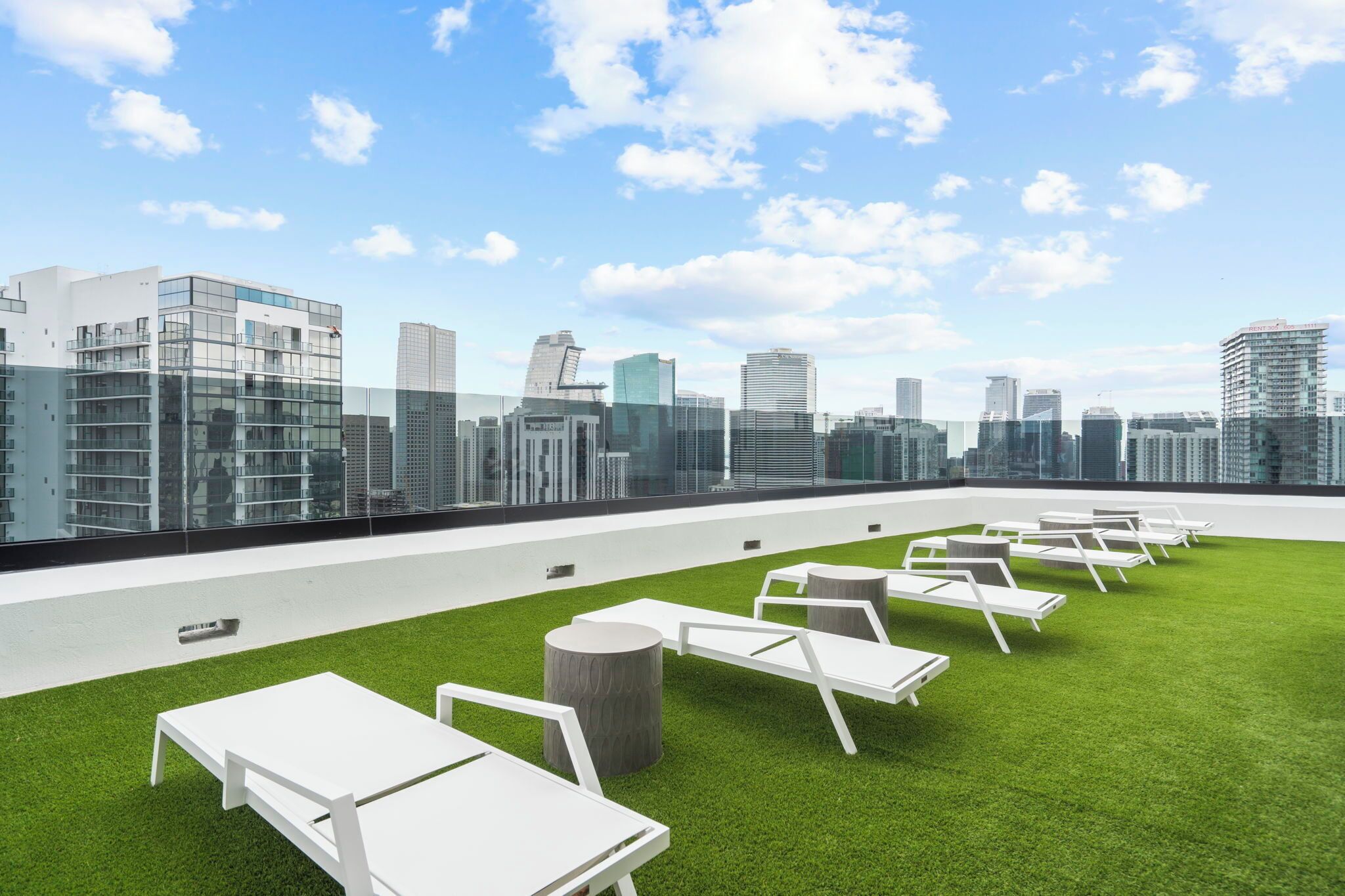 Una terrazza sul tetto con poltrone da relax bianche e un prato verde, con vista su un orizzonte cittadino caratterizzato da edifici moderni.