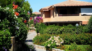 En villa med tegltag, omgivet af en have med forskellige blomster og en stenhovedvej.