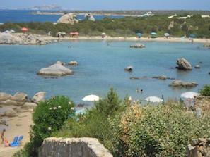A beach with clear water, rocks, and umbrellas. - DELICIOUS MONO EMY D4 (Golfo di Marinella)