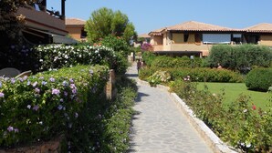 En sti der fører gennem en have med brosten, omgivet af frodig vegetation og blomstrende planter.