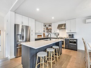 Eine moderne Küche mit weißen Schränken, einem Edelstahlkühlschrank, einer zentralen Kochinsel mit Barhocker und einem eingebauten Backofen.