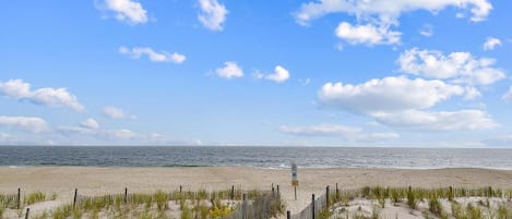 A beach path leading to the ocean with a wooden fence and dunes.