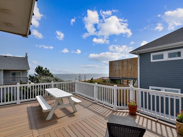 A wooden deck with a picnic table and chairs, a white railing, and a view of the ocean. - 5BR Beach Home | Steps to Ocean | Sleeps 12! (North Bethany Beach)