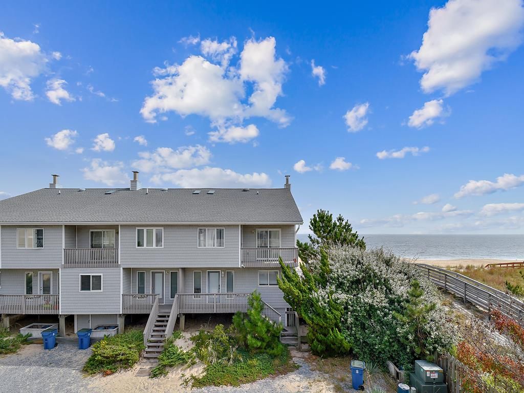 A multi-story building with a balcony on the ground floor, a staircase leading to the upper floors, and a view of the beach.