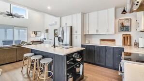 A modern kitchen with a central island, bar stools, a refrigerator, and a dining area. - 5BR Beach Home | Steps to Ocean | Sleeps 12! (North Bethany Beach)