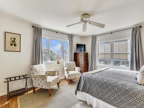 Ein Schlafzimmer mit einem Bett, zwei Sesseln, einem Schminktisch, einem Fernseher und einem Deckenventilator.