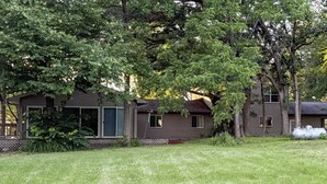 A two-story house with a front porch, surrounded by a grassy yard and trees.