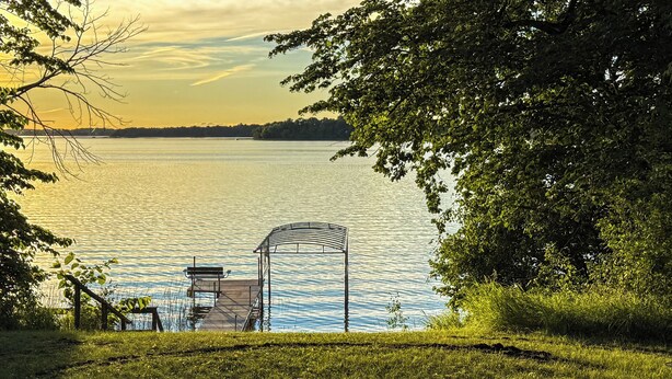 Blick auf einen See mit einem Pavillon, einer Holzsteg und einer Rasenfläche.
