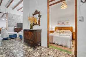 Un dormitorio con cama, cómoda, televisor y pared de piedra.