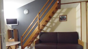 A living room with a wooden staircase, a sofa, a television, and a clock on the wall. - A 10 kms d'ANGERS small independant house 2 persons quiet countryside (Loire-Authion)
